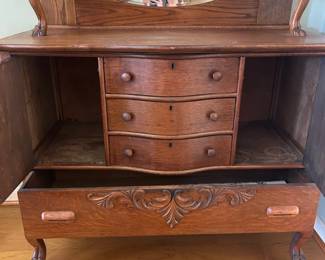 Beautiful antique solid oak hutch featuring intricate carved details, an elegant oval mirror, and rich wood grain throughout. Includes three center drawers, two side cabinets, and a large lower drawer for ample storage.