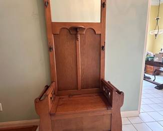 Charming antique entryway piece featuring a built-in bench, storage compartment, mirror, and multiple coat hooks. A beautiful and functional entryway piece with  warm wood character.