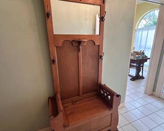 Charming antique entryway piece featuring a built-in bench, storage compartment, mirror, and multiple coat hooks. A beautiful and functional entryway piece with  warm wood character.