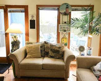 Coastal Living Room Furnishings & Nautical Décor Comfortable coastal-inspired seating group featuring a matching loveseat and sleeper sofa (hide-a-bed) upholstered in a neutral textured fabric. Includes coordinating lighthouse and nautical-themed accent pillows, making this an ideal setup for a beach house, lake home, sunroom, or Florida-style living space. Also featured throughout the room: Matching loveseat Sleeper sofa / hide-a-bed sofa Nautical and lighthouse accent pillows Decorative pelican lamp Artificial palm tree floor lamp Lighthouse wall décor Coastal wall art and framed nautical prints Ship's wheel clock Assorted beach house and seaside decorative accents A charming collection of coastal furnishings and décor that creates a relaxed waterfront atmosphere