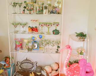 Fun tropical entertaining collection featuring hand-painted palm tree and flamingo glassware, novelty wine accessories, illuminated flamingo décor, white metal bakers rack, and matching white metal storage pieces."