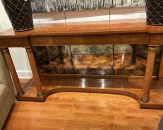 png: Burl Wood Neoclassical Style Console Table Era: Late 20th Century (Circa 1980s–1990s) – Neoclassical / Empire Revival Description: An elegant, grand-scale console table (or credenza pier table) featuring an exquisite, highly figured burl wood veneer finish. Designed with strong architectural elements, the table showcases a straight-front overhanging top supported by two striking, fluted column pillars with contrasting dark-finished bases and collars. The back features an integrated, three-panel antiqued smoke mirror backing that beautifully reflects light and adds depth to the lower display deck. A distinctively curved, concave cutout on the bottom stretcher shelf completes this statement piece, making it a perfect fit for a grand entryway, dining room, or a curated vignette. png: Estimated Dimensions Width: 64" Depth: 18" Height: 34" These dimensions reflect a grand-scale, architectural statement piece typical for an entryway console or dining room pier table.