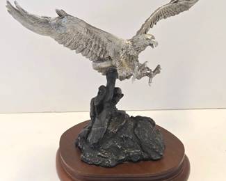 A limited edition #1153/9500 pewter sculpture of an eagle entitled "Triumphant Glory" by George De Lodzia. Issued by Chilmark Fine Pewter in 1983. 9" tall x 10" wide x 5" deep. The lot also includes a crystal paperweight with an intaglio engraved bird in flight.