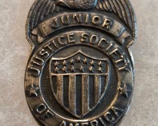 In excellent condition with great original patina.  In 1942, DC introduced the Junior Justice Society of America fan club in All-Star Comics #13. The Justice Society of America was the first superhero team in comic book history. For 10 cents, a child received a club member kit that included a welcome letter, a decoder wheel, a membership card, a miniature comic book and THIS stamped metal badge. The badge, especially in this condition, is very rare, as it was only produced for two months before being discontinued due to metal rationing in World War 2. The metal badge measures 1 1/2" tall and 7/8" wide.