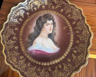 This vintage plate is a Bavarian reproduction of a Royal Vienna portrait plate, typically featuring a burgundy border with elaborate gold accents.
