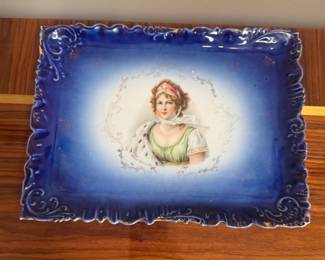 This vintage porcelain portrait tray features a hand-painted scene of a woman with a cobalt blue scalloped edge.