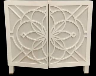 328 - Chelsea House Flower of Life Cabinet (Description): white, 36 x 38 x 21, need some work on doors, The Flower of Life Cabinet features a stunning lattice overlay crafted from sturdy white wood, creating an intricate pattern that adds depth and dimension to the piece. Set against the backdrop of natural raffia, the lattice design exudes a sense of coastal-inspired allure, evoking images of breezy beachfront retreats and sun-kissed shores. Designed by Lisa Kahn.