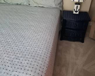 Queen bed with wicker headboard matches 7-drawer dresser; matching nightstand; table lamp