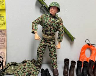 Closeup of the incredible rare vintage 1964 G.I. JOE action figure with multiple outfits (including camouflage, sailor, dress uniform, soldier, et al) and supplies including combat trailer, helmets, rifles, ammo belts, boots, underwater diving helmet, stretcher, lifejacket, and comes with original 1960s Hasbro G.I. Joe Action Soldier toy catalog.The poster features available action figures and their accessory sets for the 1964 catalogue year, including Army, Navy, Air Force, and Marine branches.