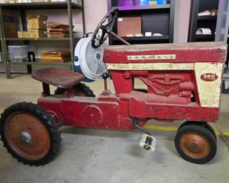 A vintage McCormick Farmall 560 pedal tractor. This specific model is a collectible die-cast metal toy that replicates the full-sized row-crop tractor produced by International Harvester between 1958 and 1963.