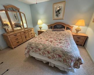Complete queen bedroom suite in light oak with decorative wrought iron lattice insets on the headboard and dresser mirror frame. Includes: arched headboard, large dresser with triple mirror, and two matching nightstands. Brass bail pulls throughout. 1990s–2000s American traditional style in good condition.