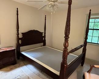 Dramatic queen-size four-poster bed in dark mahogany with heavily carved and rope-twist posts topped with pineapple finials. Carved arched headboard with scrollwork detail. Traditional American Colonial/Chippendale style. Very substantial and visually impressive piece. No mattress.