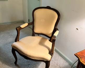 French Provincial / Louis XV style open armchair (fauteuil) with carved walnut-stained wood frame, cabriole legs, and cream/ivory upholstery. Classic scalloped cartouche back. Upholstery shows wear and some separation at the armrests — a reupholstery candidate but the frame is excellent.