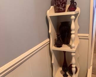 White vintage corner shelf with collection of ruby glass