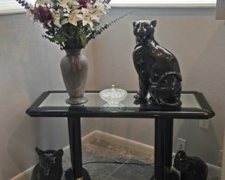 Black and glass couch table with ceramic cats and a flower arrangement