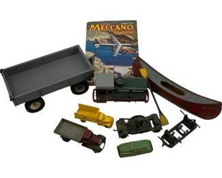 1188 - Antique Toy Vehicles, Canoe & Meccano (Description): Lot of antique toys including a collection of vintage toy vehicles and a tin canoe. The grouping features a large gray metal trailer on wheels, a green and gray delivery truck, a maroon sedan, a yellow construction vehicle, a green vintage car, and additional vehicle parts. Also included is a painted tin canoe marked 'USA' with red exterior and yellow interior, complete with a small paddle. The lot is accompanied by a February 1957 Meccano