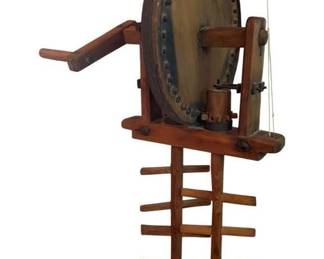 70 - Ant. Handcrafted Primitive Wooden Rope Maker (Description): Antique wooden handcrafted primitive rope making device, possibly a rope melting apparatus or foliot clock mechanism. This rustic piece features a large circular wooden wheel with evenly spaced pegs around the perimeter, mounted on a sturdy wooden frame with a hand crank for manual operation. The base includes a ladder-style spool rack for holding rope or twine. Constructed entirely of wood with iron hardware and fittings,