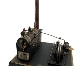 19 - Doll et Cie Stationary Steam Engine Model (Description): Doll et Cie 1920s stationary horizontal steam engine model featuring a cylindrical boiler housed within a brick-patterned firebox, a tall faux-brick smokestack, and a connected flywheel engine assembly. The model is mounted on a black-painted metal base with gilt trim edging. Measures 15 1/2" x 12" x 10".