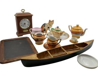 144 - Group Lot of Asian Decor & More (Description): A diverse group lot featuring Asian-inspired decor and collectibles. The lot includes a wooden mantel clock with brass ring handle and Roman numeral face, a decorative wooden canoe model with black painted hull, a vintage slate writing board in wooden frame, Japanese lusterware tea set pieces including teapot, sugar bowl, and creamers with hand-painted landscape scenes, a ceramic cat figurine, porcelain serving pieces with