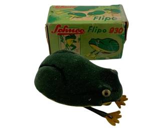 1216 - Schuco Flipo 930 Wind-Up Frog Toy w/ Box (Description): Schuco Flipo 930 wind-up frog toy with original box. The vintage German-made mechanical frog features a dark green velvet body with gold-tone metal feet and glass eyes. The clockwork mechanism is operated by a wind-up key. Includes the original illustrated cardboard box with Schuco branding. Used as is electric/electronic/mechanical item. No guarantee all components, untested.