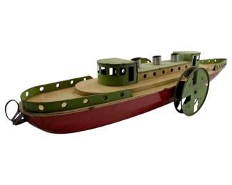 12 - Bettsy Green Boat 5"x26"x7" (Description): Bettsy Green Boat, a charming vintage-style painted tin paddlewheel steamboat model. Features a red hull with cream and green painted deck details, twin smokestacks, pilot house, and decorative side paddle wheels. The boat displays characteristic folk art qualities with its hand-painted finish showing gentle age wear. Measures 5" x 26" x 7".