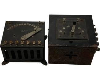 1230 - 2pc Lot Voltamp Train Transformers 5"x6"x7" (Description): Two-piece lot of antique Voltamp train transformers. These early 20th century electrical control units feature black metal casings with dial controls, brass terminals, and rotary switches on top. One unit displays ventilation slots on the base, while the larger unit shows a cross symbol on the front panel. Both units show age-appropriate patina and wear consistent with their vintage. Measurements: 5" x 6" x 7".
