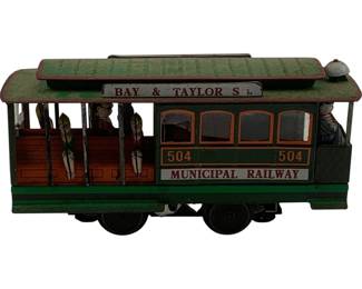 1119 - Tin Litho Municipal Railway Trolley Car Toy (Description): Tin lithographed trolley car toy depicting a San Francisco Municipal Railway cable car. The car is numbered 504 and features "Bay & Taylor St." and "Municipal Railway" signage. Painted in classic green with orange trim, the trolley includes lithophed passengers and a conductor figure. The open-air design shows bench seating and detailed window frames. Measures 4 1/2" x 7" x 2.5".