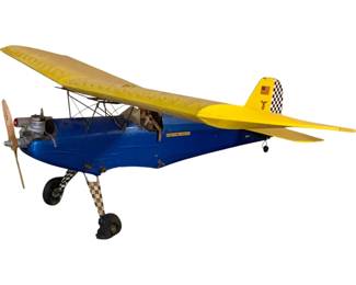1108 - Gas Powered Model Plane 17"x48"x10" (Description): Gas powered model airplane featuring a blue fuselage with yellow wings and tail section. The aircraft includes a checkered pattern on the tail fin and landing gear struts, with an American flag decal on the vertical stabilizer. The model is equipped with a front-mounted engine and wooden propeller, open cockpit with pilot figure, and fixed landing gear. Measures 17 inches high by 48 inches long by 10 inches wide. Sold as-is.