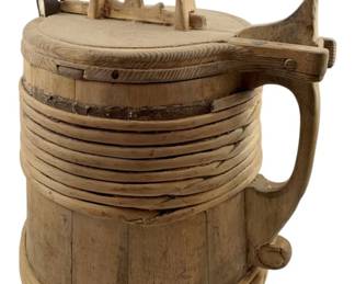 60 - 19th Century Scandinavian Wooden Tankard (Description): A 19th century Scandinavian wooden lidded tankard featuring traditional stave construction with horizontal banding around the upper portion. The tankard has a hinged lid with a carved arched handle on top, a carved pouring spout, and a sturdy integral handle on the side. The piece displays characteristic Nordic craftsmanship with its turned wooden bands and metal reinforcement around the lid hinge. Measures 11" x 9" x 8".