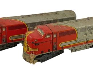 495 - 2pc. Santa Fe Locomotives (O Scale) 4"x13"x3" (Description): Two Santa Fe locomotives in O Scale. The pair features classic Santa Fe livery with red and silver coloring. Each locomotive measures 4 inches high by 13 inches long by 3 inches wide.