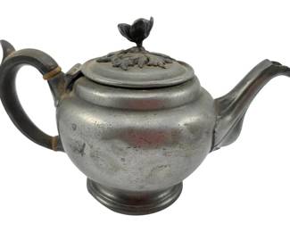 132 - Vtg Pewter Teapot w/ Floral Shaped Finial (Description): Vintage pewter teapot featuring a decorative floral shaped finial atop an ornate lid with acanthus leaf relief design. The teapot has a classic bulbous body with a curved spout and C-scroll handle. The piece shows a lovely aged patina consistent with its vintage character. Measures 4 1/2"x7"x4".