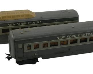 883 - 2pc Lot Marx Tin Litho Passenger Cars (Description): Two-piece lot of Marx tin lithograph passenger cars marked "New York Central" with car number 234. The gray passenger cars feature printed windows with passenger silhouettes. One car appears to be a coach car while the other has an observation domed top. Each car measures 3.5 inches by 11 inches by 2 inches.