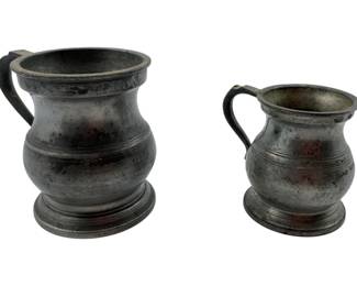 129 - Vtg Pewter Birmingham Tankards (Description): Vintage pewter Birmingham tankards featuring classic baluster-shaped bodies with curved handles and footed bases. This pair includes two differently sized tankards, each displaying the characteristic aged patina of antique pewter with warm undertones. Measures 3" x 3.5" x 2.5".