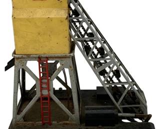 940 - Lionel Coal Elevator 11.5"x10"x7" (Description): Lionel coal elevator model train accessory. This vintage tinplate piece features a yellow tower structure with red roof and ladder, supported by metal framework with an angled conveyor mechanism mounted on a black base. Measures 11.5 inches by 10 inches by 7 inches.