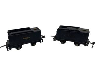 322 - 2 Lionel Train Cars 3"x2"x8" (Description): Two vintage Lionel train cars in dark blue/black painted metal construction. The set includes a coal tender and a locomotive tender car, both featuring the classic Lionel nameplate. Each car measures 3 inches high by 2 inches wide by 8 inches long. The cars display traditional pressed steel construction with simulated rivet detailing and original couplers for connecting to other rolling stock.