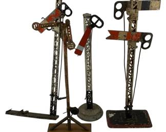 1186 - 4pc O Scale Train Signal Accessories (Description): A collection of four O scale train accessories featuring vintage-style railway semaphore signals. The lot includes three lattice-tower signal posts with articulated semaphore arms painted in red and white, each mounted on metal bases. The signals display characteristic period detailing with spectacle plates and operating mechanisms typical of early model railroad accessories. The pieces show aged patina consistent with