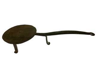 67 - Ant. Hand Forged Wrought Iron Spider Pan (Description): Antique hand forged wrought iron "spider" pan, a traditional three-legged cooking vessel designed for use over open hearths. The pan features a flat circular cooking surface supported by three curved legs, with a long handle terminating in a hanging loop. The piece displays a dark patina consistent with age and use. Measures 3 1/2" x 21" x 8".