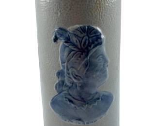 87 - Old Sleepy Eye Cattail Stoneware Vase (Description): Old Sleepy Eye cattail stoneware vase featuring a cobalt blue relief portrait of an Indigenous woman in profile against a gray salt-glazed body. The cylindrical vase displays the characteristic textured surface with decorative geometric bands at the rim and base. Measures 8.5" x 3.5".