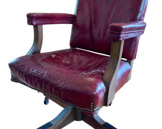 38 - Vintage Rolling Desk Chair (Description): Featuring rich burgundy upholstery with nailhead trim detailing along the seat edge. The chair has padded armrests supported by a curved wooden frame. Set on a four-leg wooden base with caster wheels for mobility. Measures 36 inches high by 23 inches wide by 23 inches deep, with arm height at 27.5 inches.