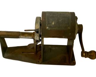 1046 - Vtg Hand Crank Pencil Sharpener (Description): Vintage hand crank pencil sharpener featuring a metal construction with a rotating barrel mechanism and wooden handle. The sharpener is mounted on a flat metal base with mounting holes for desk or table installation.