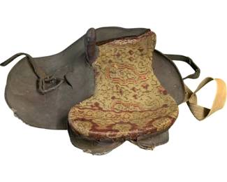 1136 - Antique Horse Saddle 12"x26"x22" (Description): Antique horse saddle featuring a leather body with a decorative tapestry-style upholstered seat. The seat displays a traditional woven pattern in muted gold, burgundy, and coral tones. The saddle includes leather straps and a wooden stirrup. Shows age-appropriate wear consistent with use. Measures 12 inches by 26 inches by 22 inches.