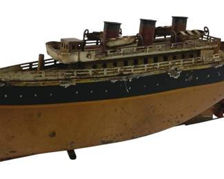 879 - Antique Tin Litho Steam Ship 4.5"x11"x2.5" (Description): Antique tin lithograph steam ship toy measuring 4.5" x 11" x 2.5". This four-funnel ocean liner features a painted hull in ochre, black, and cream with yellow accent stripes. The deck includes detailed railings, portholes, and ventilation stacks. The ship shows honest age wear consistent with its vintage, including paint loss and patina. Mounted on small wheels for display or play.