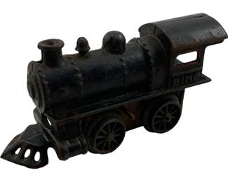 1082 - Antique O Scale Cast Iron Locomotive (Description): Antique O scale locomotive crafted from cast iron with a black painted finish. This charming toy train features classic steam engine details including a smokestack, bell dome, cow catcher, and open cab windows. The locomotive shows desirable age-related patina with some paint wear revealing the iron beneath. Measures 10 inches long by 6 inches wide by 8 inches tall.