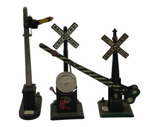 863 - 3 Pc Lot Vtg Railroad Crossing Signals (Description): A three-piece lot of vintage railroad crossing signals in O scale. The collection includes two railroad crossing signs with the classic X-shaped crossbuck design reading "Railroad Crossing," along with a semaphore signal and a crossing gate mechanism. The pieces feature painted metal construction with black bases and striped crossing arms. These vintage model train accessories show period-appropriate wear consistent with their