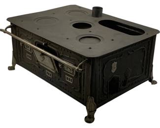 1117 - Metal Salesman Sample Stove (Not Complete) (Description): Metal salesman sample stove in black finish, featuring a cast iron construction with decorative claw feet. The miniature stove includes multiple burner openings on the top surface, a central stove pipe, and front-opening doors with ornate detailing and a horizontal towel bar. This piece is not complete. Measures 10.5 inches.