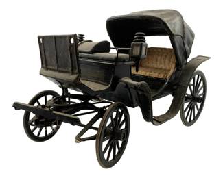 6 - Vintage Woodmade Carriage 8"x11.5"x6" (Description): Vintage woodmade carriage model featuring detailed craftsmanship with a black painted finish. The piece includes a folding leather-style canopy top, tufted tan upholstered seating, working spoke wheels, and a driver's bench seat. A small lantern detail is mounted on the side. The carriage measures 8 inches by 11.5 inches by 6 inches.