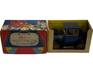 1211 - Schuco Oldtimer 1917 Ford Coupe T w/ Box (Description): Schuco Oldtimer 1917 Ford Coupe T model car with original box. This vintage diecast model features a blue body with black roof and tan spoke wheels. The car is presented in its colorful illustrated Schuco 1227 series box depicting a theatrical stagescene with classic automobiles. Model is in displayed condition within its original packaging.