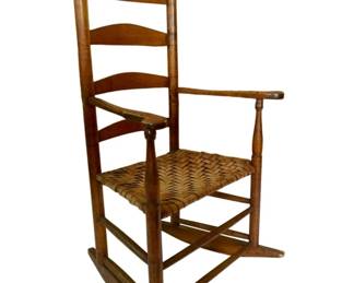 52 - Vtg Ladderback Rocking Chair 45.5"x24"x19" (Description): Vintage wooden ladderback rocking chair featuring a woven splint seat. The chair displays classic American country styling with three curved slats forming the ladder back, acorn-style finials atop the rear posts, and shaped wooden arms. The warm-toned hardwood construction shows attractive patina consistent with age. Measures 45.5"x24"x19".