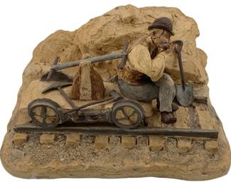 1031 - Plaster Sculpture 8"x6"x4" (Description): A plaster sculpture depicting a seated figure with a shovel and wheeled cart on railroad tracks. The piece measures 8 inches by 6 inches by 4 inches.