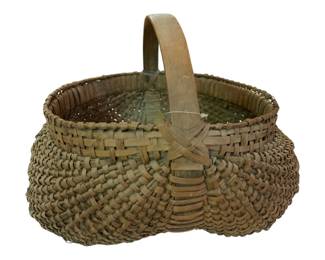 74 - Henry Co Primitive Woven Basket w/ Handle (Description): Henry County primitive basket featuring a bent wood handle and traditional woven splint construction. The basket displays a classic buttocks or egg basket form with a rounded, bulbous shape tapering at the base. The natural patina and handcrafted weave pattern are characteristic of American folk art basketry. Measures 12" x 15" x 13".